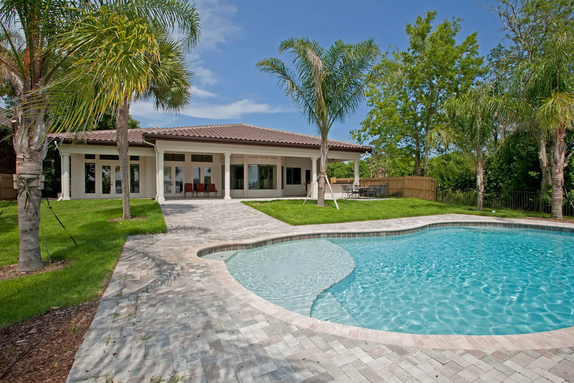 A Mediterranean-style home outdoor living area with pool, patio and landscape architecture with palm trees by Ben Butera.