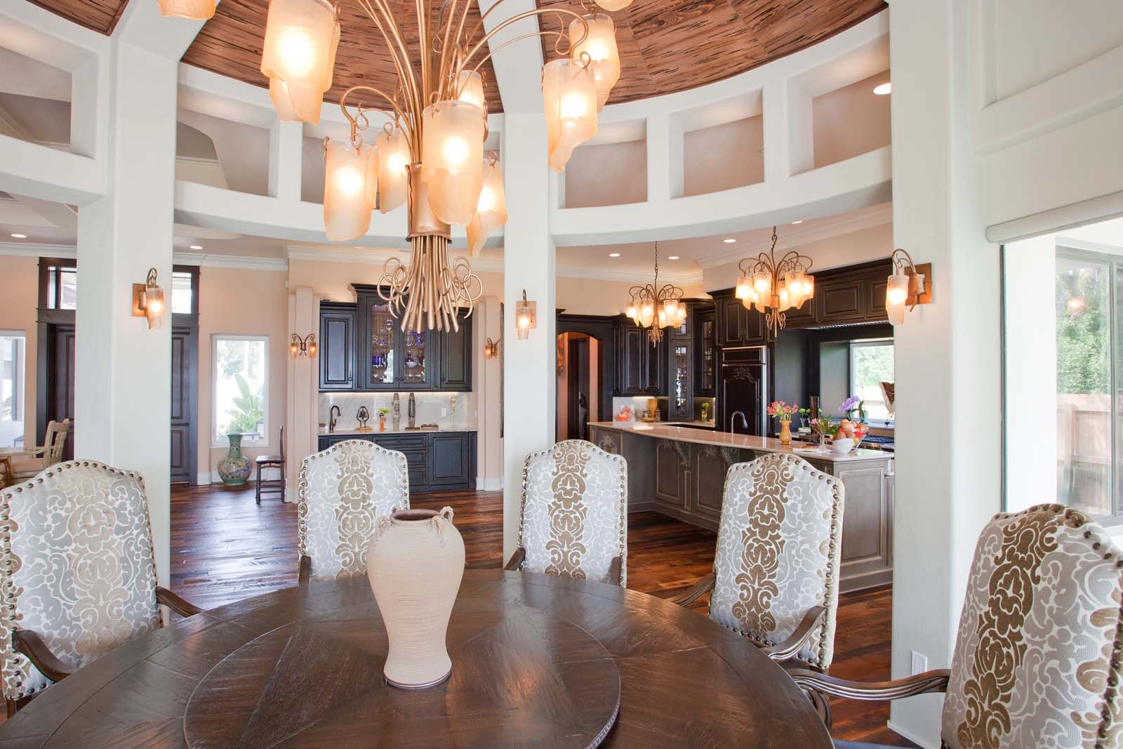 Dining area with ceiling detail and chandelier surrounded by columns next to a chef’s kitchen by architect Ben Butera.