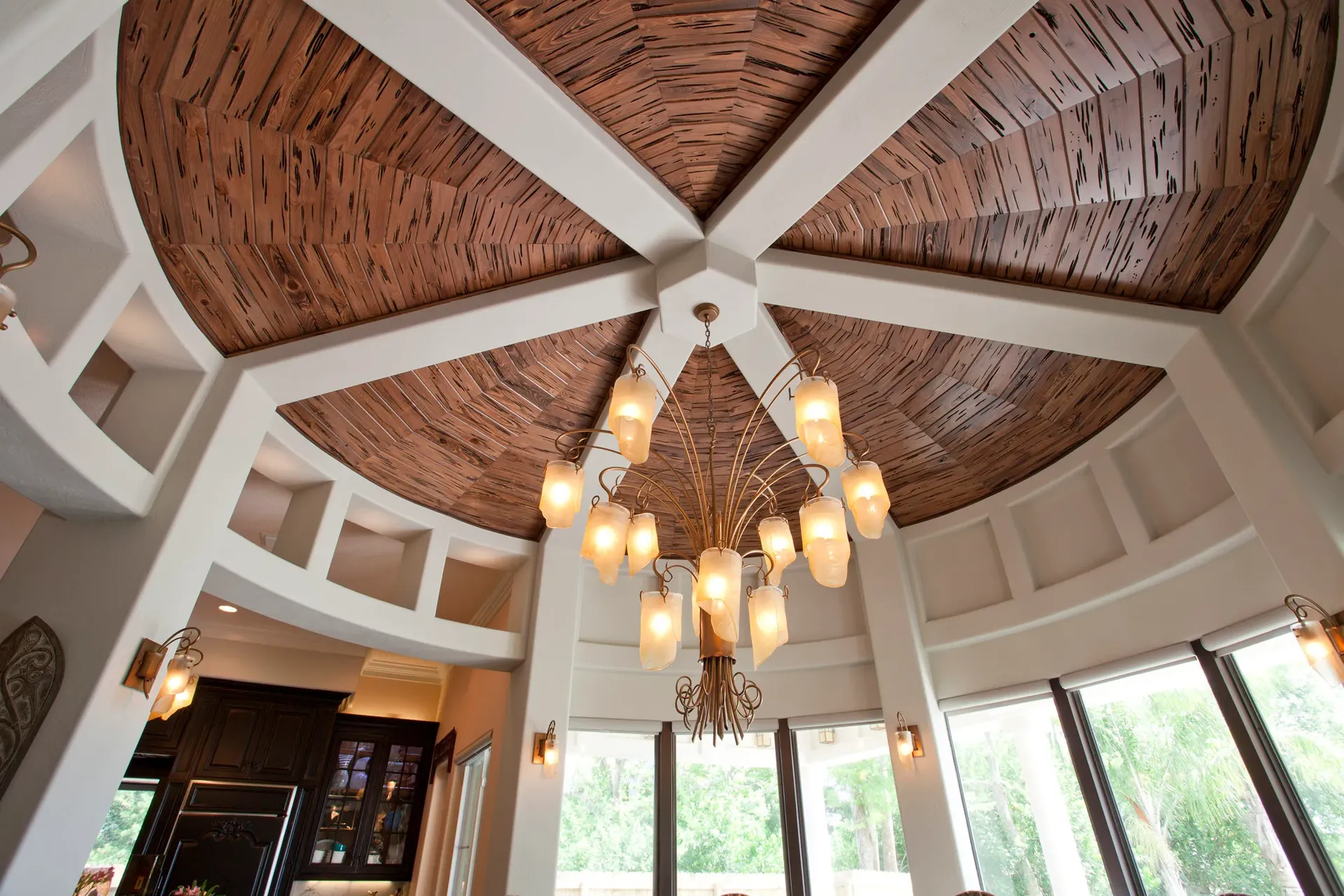 Butera Designs round wooden ceiling and elegant chandelier, framed by curved walls and large windows for natural light.